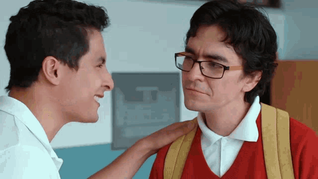 a man wearing glasses talks to another man in a red shirt
