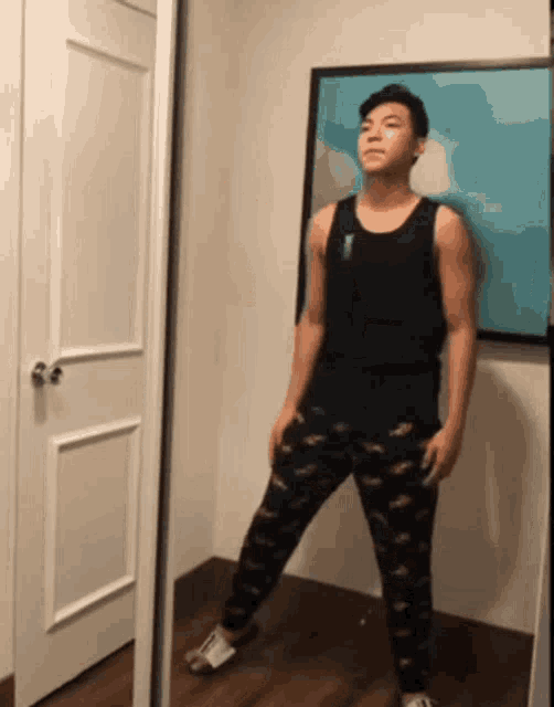 a man standing in front of a mirror wearing a black tank top and black pants