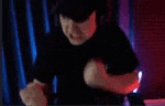 a man in a black shirt is making a fist gesture in front of a red curtain .