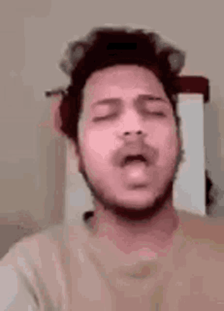 a young man with a beard is yawning with his eyes closed .