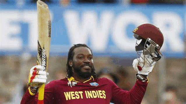 a cricket player is holding a bat and a helmet in his hands .