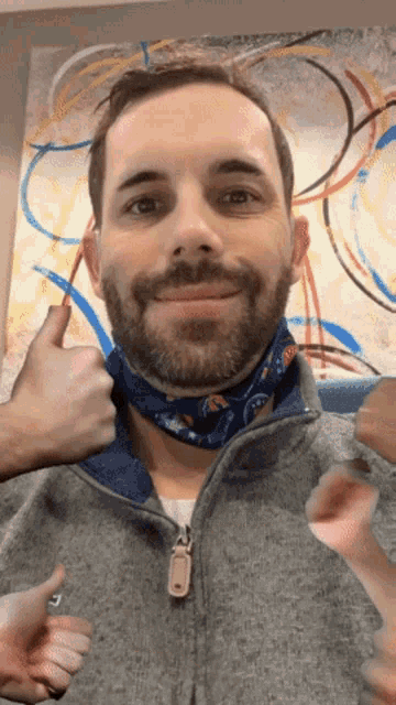 a man with a beard wearing a bandana around his neck gives a thumbs up