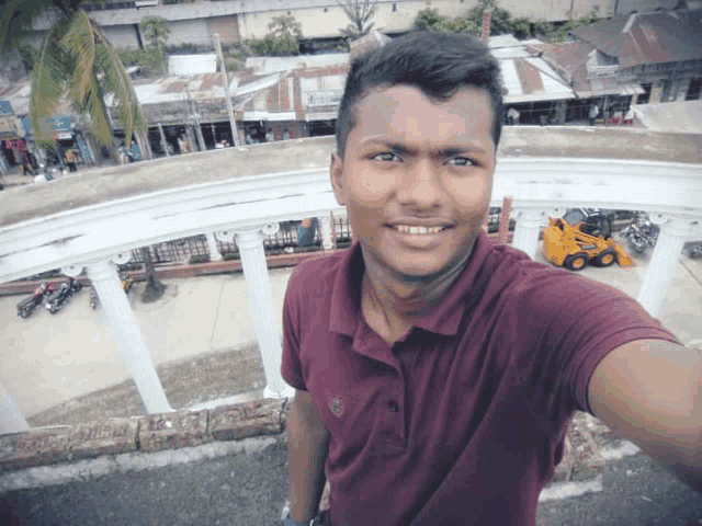 a man in a maroon shirt takes a selfie in front of a building that says ' a ' on the front