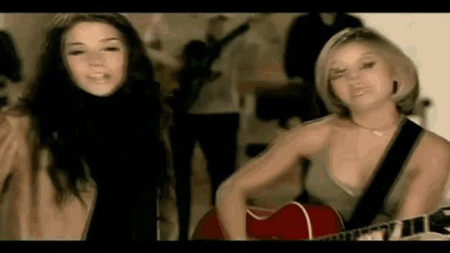 two women are standing next to each other playing guitars .