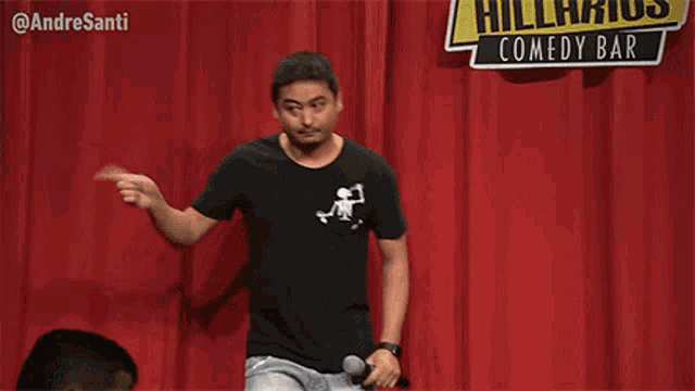 a man is standing in front of a red curtain holding a microphone and pointing at something .