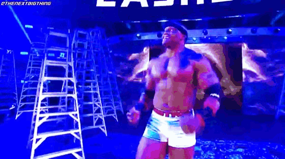 a wrestler is standing in front of a blue wall with the word last on it .