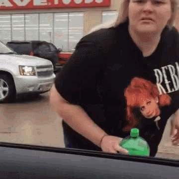 a woman wearing a black rebel t-shirt is holding a green bottle