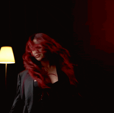 a woman with red hair is standing in front of a lamp in a dark room