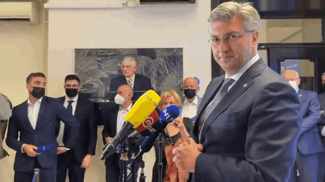a man in a suit stands in front of several microphones including one that says ' n1 '