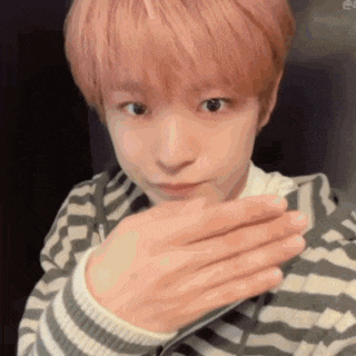 a young boy with pink hair is covering his mouth with his hands .