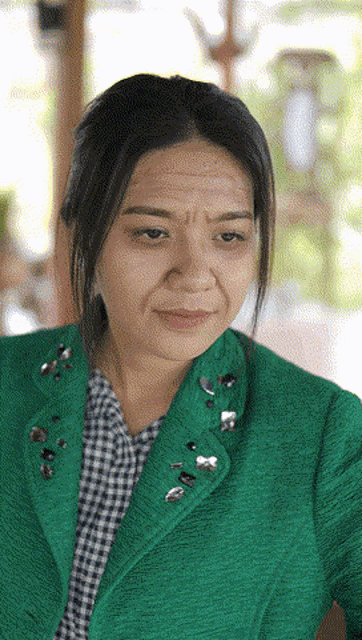 a woman wearing a green jacket and a plaid shirt is making a funny face