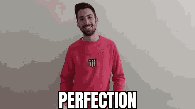 a man with a beard is wearing a red sweatshirt and smiling while standing in front of a wall .