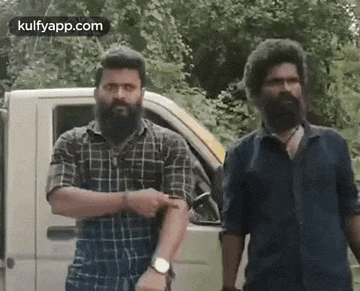 two bearded men are standing next to each other in front of a truck .