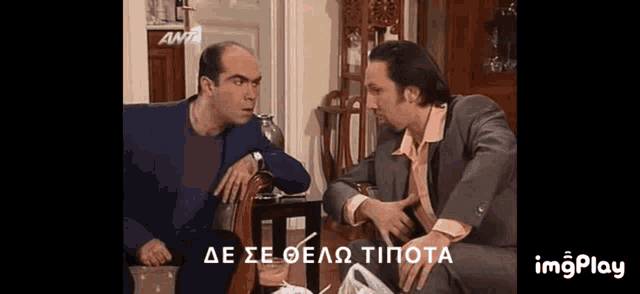two men are sitting next to each other in a living room and talking in greek .