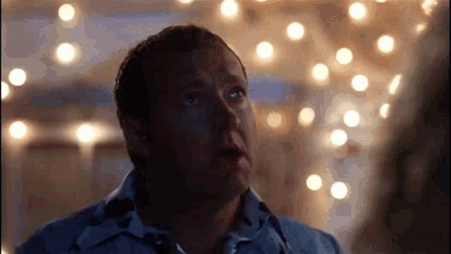a man in a blue shirt is standing in front of a string of lights