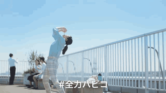 a woman stands on a balcony with a blue sky in the background and the hashtag # on the bottom right