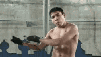a shirtless man is standing in a gym holding a pair of boxing gloves .