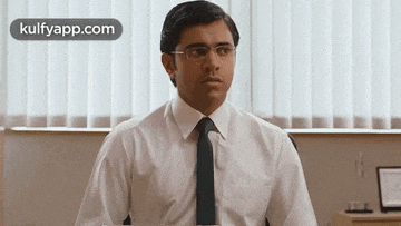 a man in a white shirt and black tie is sitting at a desk in front of a window .