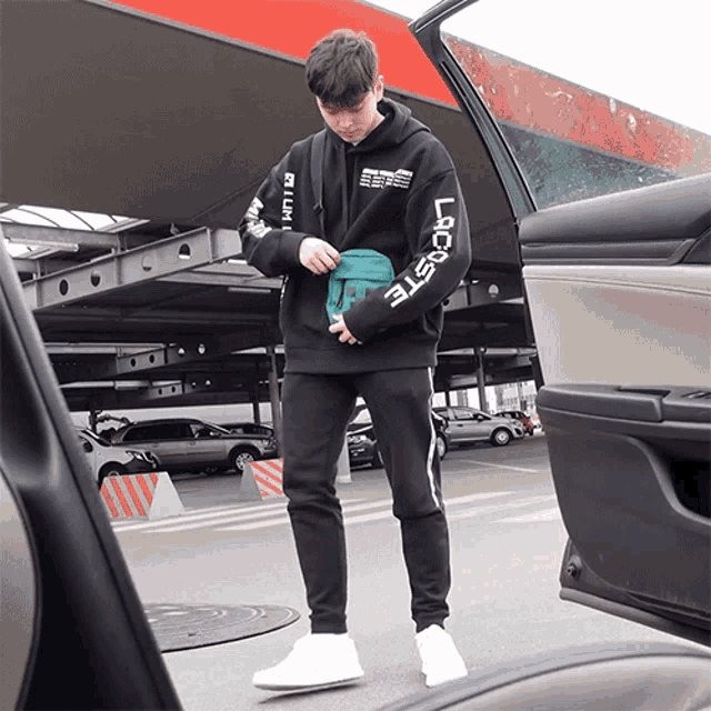a man wearing a black lacoste hoodie holds a blue bag