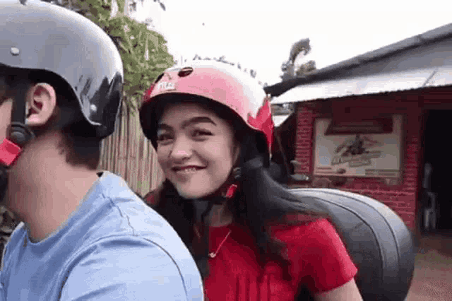 a woman wearing a red helmet is sitting on the back of a man 's motorcycle .