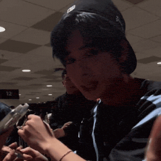 a young man with blue hair is holding a cell phone in his hand in a crowded room .