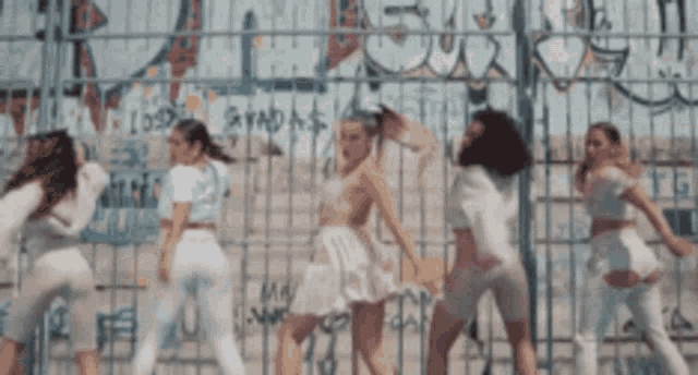 a group of girls are dancing in front of a fence with graffiti on it .