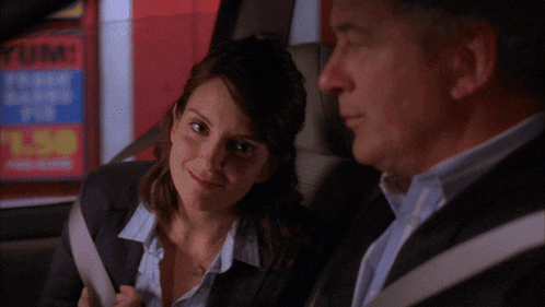 a man and a woman are sitting in a car with a sign in the background that says yum
