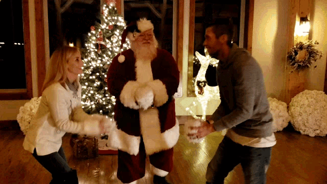 a man and a woman are standing next to santa claus in front of a christmas tree