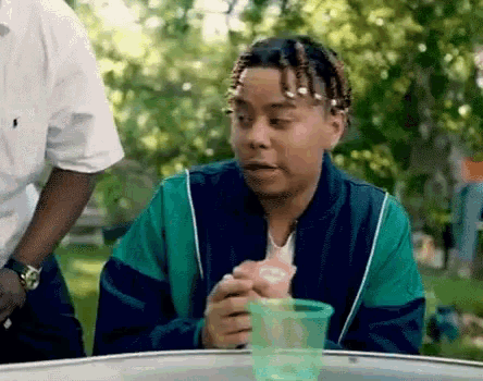 a man in a green jacket is sitting at a table eating an ice cream cone from a green cup