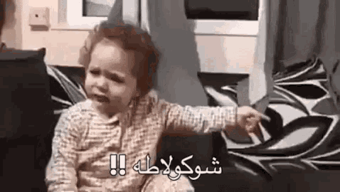 a baby is crying while sitting on a couch and pointing at the camera .
