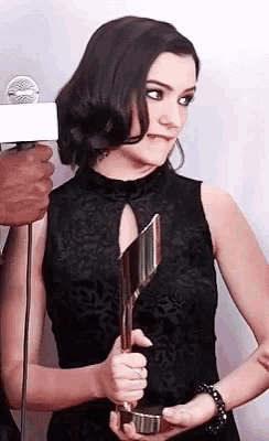 a woman in a black dress is holding a trophy in her hands .