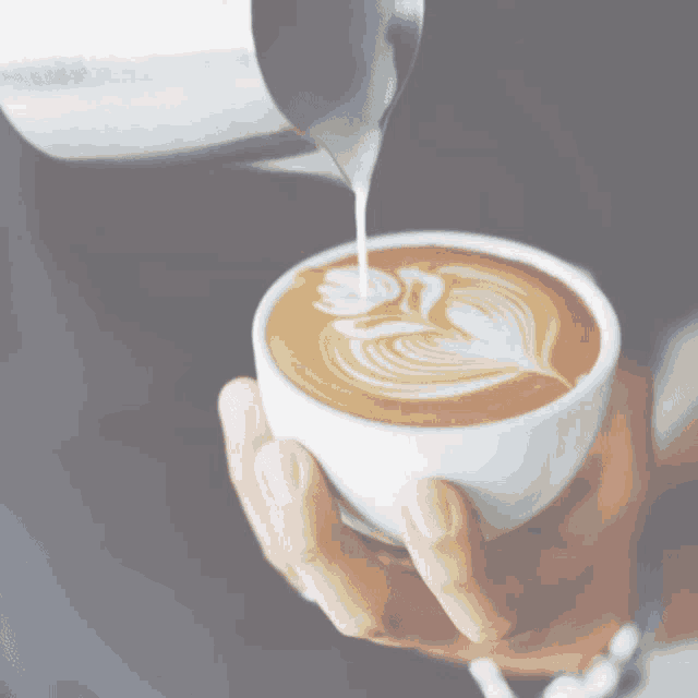a person pouring milk into a cup of coffee with a yellow g on their shirt