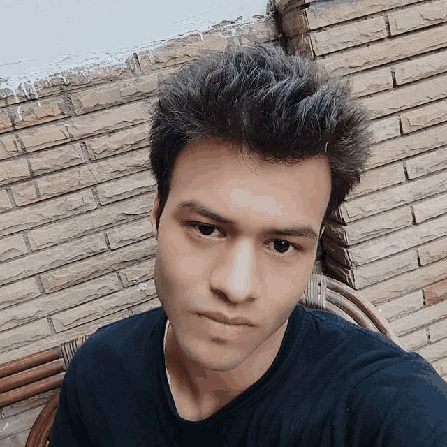 a young man taking a selfie with a brick wall behind him