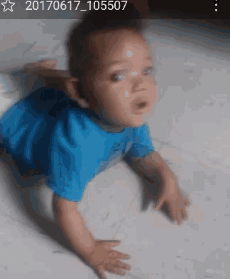a baby in a blue shirt is crawling on the floor in a photo taken in 2017