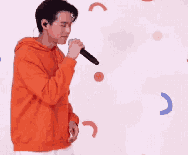 a man in an orange hoodie is singing into a microphone .