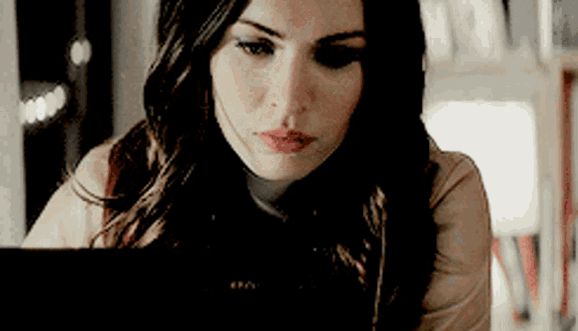 a woman with long dark hair is looking at her laptop screen