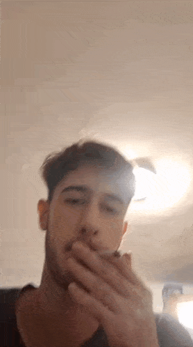 a young man with a beard is smoking a cigarette in a room .