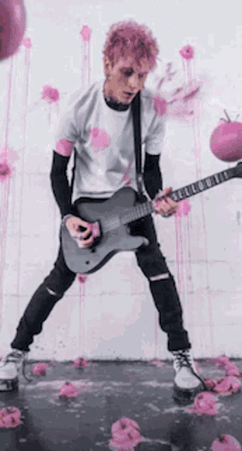 a man with pink hair is playing a guitar in front of a wall covered in pink flowers .