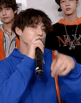 a young man in a blue hoodie is holding a microphone and pointing at something .
