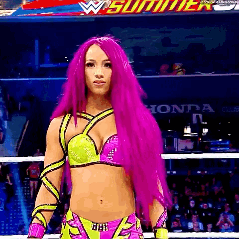 a female wrestler with pink hair is standing in a ring .