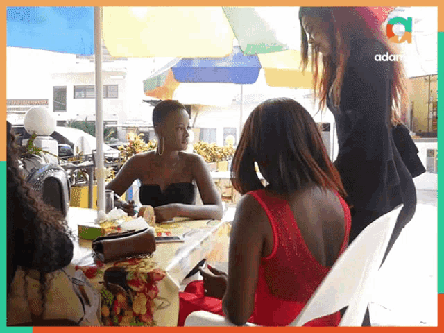 a woman in a red dress sits at a table next to a woman in a black top