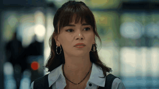 a woman wearing hoop earrings and a necklace looks serious