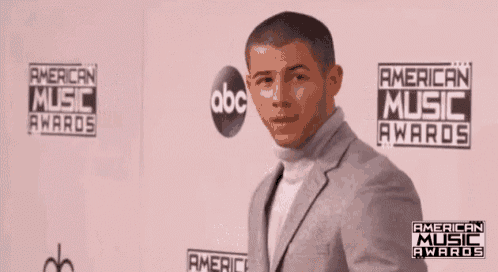 a man is standing in front of a wall that says american music awards on it