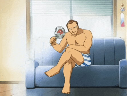 a shirtless man sits on a couch holding a fan that says ' r ' on it