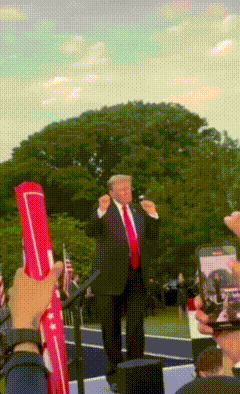 a man in a suit and tie stands in front of a crowd holding a red flag