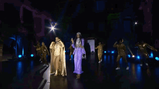a woman in a purple and gold outfit is singing on a stage