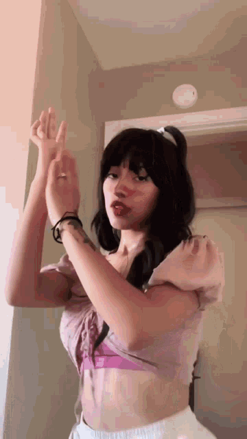 a woman in a pink top and white shorts is making a heart with her hands