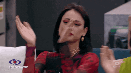 a woman in a red dress is sitting in front of a sign that says grandefratello on it