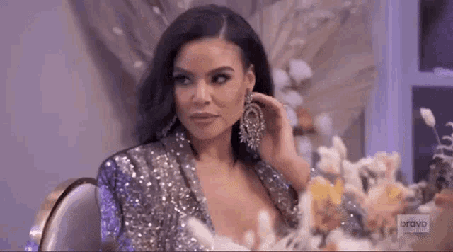 a woman in a sequined dress is sitting at a table wearing earrings .