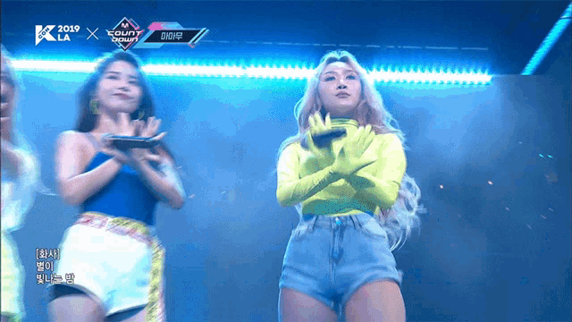 a woman in a neon yellow top stands on a stage in front of a screen that says 2019